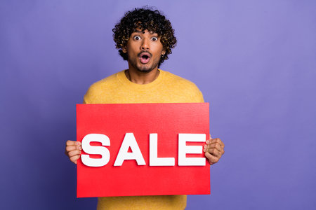 Photo of glad nice man wear trendy yellow clothes arms hold red placard sale news isolated on purple color backgroundの写真素材