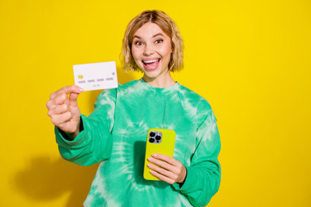 Photo of adorable excited girl wear tie dye sweatshirt showing credit card modern device empty space...