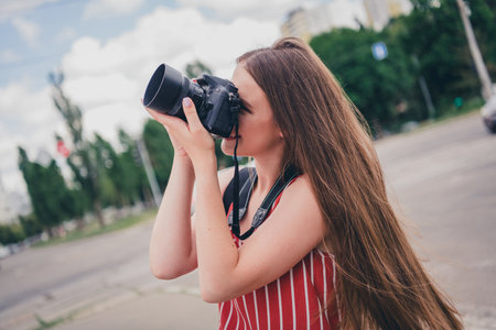 Photo of lovely adorable girl photographer amateur trendy clothes photographing taking pictures photos outdoorsの写真素材