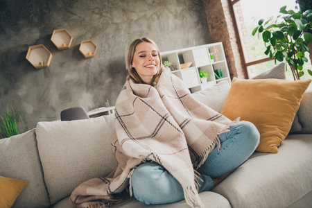 Photo of young smiling blonde hair woman wrapped soft plaid sitting on couch indoors living room...
