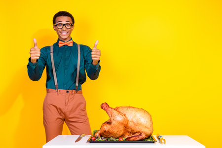 Photo of positive guy make thumb up recommend tasty turkey for thanksgiving day isolated yellow color backgroundの写真素材