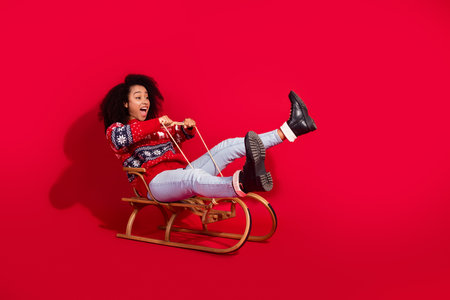 Full length photo of charming positive girl wear print sweater riding sledges celebrating xmas empty space isolated red color backgroundの写真素材