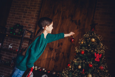 Photo of nice little girl decorate tree wear green christmas clothes enjoy cozy x-mas party decoration interior flat indoorsの写真素材