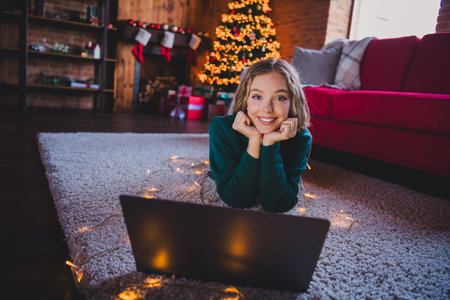 Full body photo of nice teen girl lying netbook dreamy wear green christmas clothes enjoy cozy x-mas party decoration interior flat indoorsの写真素材
