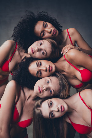 No filter photo of different nationalities women together on gray concrete wall background in studio