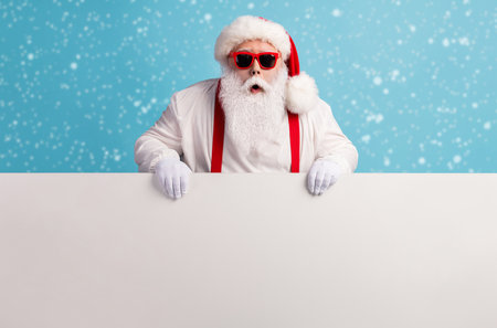 Portrait of his he nice attractive funky amazed stunned white-haired Santa holding in hands copy space board advert ad attention isolated over bright vivid shine vibrant blue color backgroundの写真素材