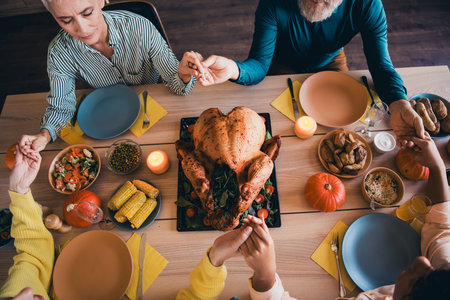 Above view cropped portrait of big friendly family hold arms pray celebrate thanksgiving day dinner flat indoors
