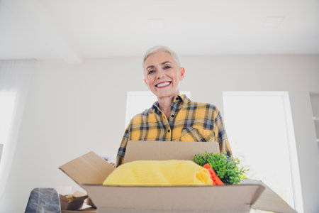 Portrait of pretty aged lady toothy smile hold box wear plaid shirt relocate move new flat indoors
