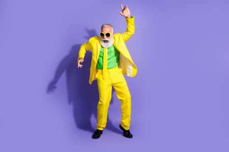 Photo of overjoyed optimistic funny senior man wearing trendy yellow clothes enjoy vacation isolated on purple color backgroundの写真素材