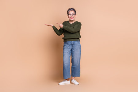 Photo of lovely senior lady wear green stylish clothes demonstrate empty space offer isolated on beige color backgroundの写真素材
