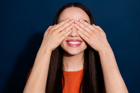 Photo of cheerful glad funny cute woman wear orange stylish clothes hide eyes isolated on dark blue color backgroundの写真素材