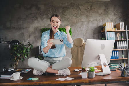 Photo of lucky positive lady broker wear shirt eyeglasses sitting table winning game modern gadget indoors workplace workshopの写真素材