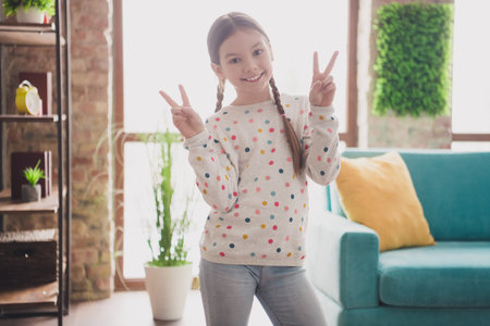 Portrait of charming little girl demonstrate v-sign wear pullover modern interior flat indoorsの写真素材