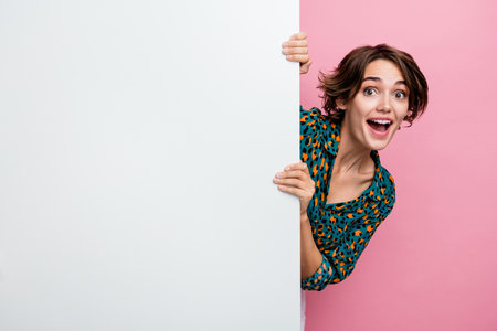 Photo of impressed friendly girl with bob hair dressed stylish shirt look out from billboard empty space isolated on pink color backgroundの写真素材