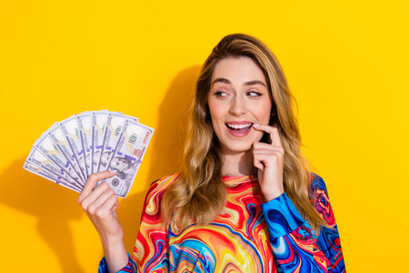 Photo portrait of pretty young girl look money fan interested wear trendy colorful outfit isolated on yellow color backgroundの写真素材