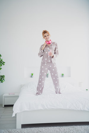 Full body vertical portrait of pretty young girl headphones phone comfy bed wear pajama bedroom apartment indoorsの写真素材