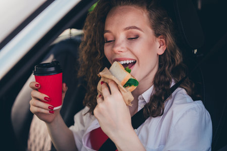 Photo of shiny attractive lady driver dressed white shirt eating snack drinking coffee gas station...