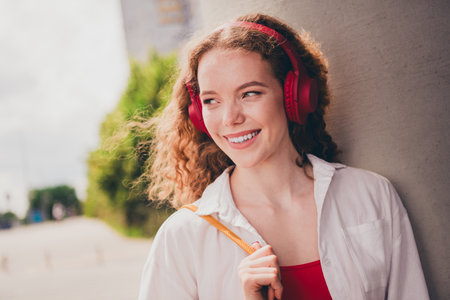 Photo of excited dreamy lady headphones listen music look empty space wear white shirt walking outside modern urban city streetの写真素材