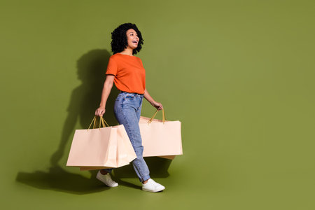Full size photo of pretty young woman mall bags walk empty space wear t-shirt isolated on khaki color backgroundの写真素材