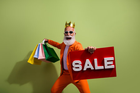 Photo of funny showman golden crown hold sale placard bags wear orange suit isolated on green color backgroundの写真素材