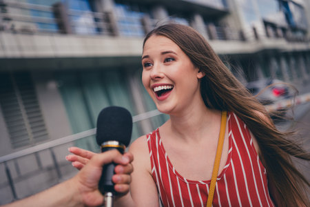 Photo of lovely cheerful popular girl giving interview answering to journalist speaking in microphone outdoorsの写真素材