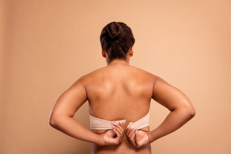 Photo of lovely pretty girl back view unfasten bra open shoulders isolated on beige pastel color backgroundの写真素材