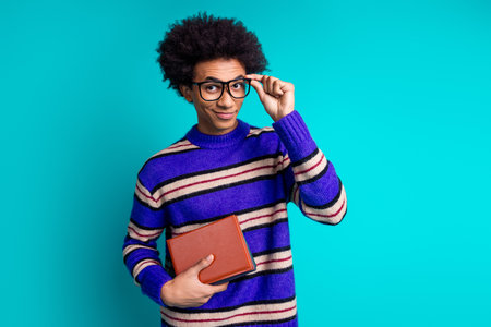 Photo of clever man guy with wavy hairstyle dressed knitwear sweater touching glasses holding book isolated on blue color backgroundの写真素材