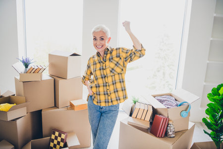 Photo of nice aged woman raise fists wear checkered shirt relocate move new apartment indoorsの写真素材