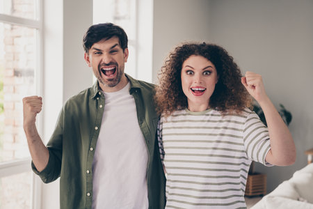 Photo of two young people raise fists shout yes modern interior apartment indoorsの写真素材