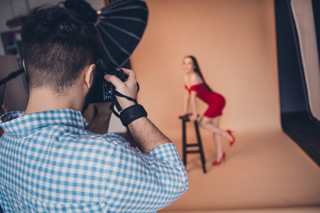 Fashion photographer taking photo of young woman in sexy red dress photo session in modern studio indoorsの写真素材