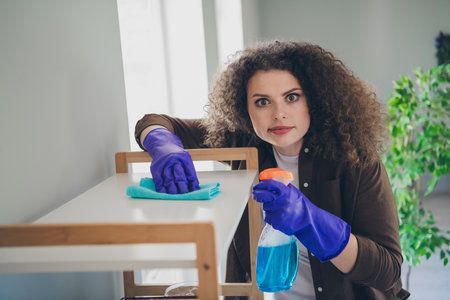 Photo of beautiful house wife young smiling woman in casual shirt using soft rag cleaning surfaces indoors comfortable loft apartmentの写真素材