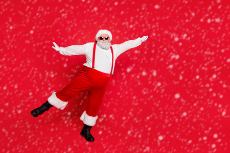 Full length photo of fat overweight hipster santa claus with big funny belly hold hand catch sleighs parasol wearing eyeglasses trousers pants isolated over red backgroundの写真素材