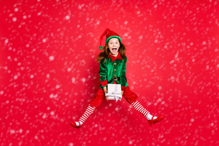 Full length body size profile side view of nice attractive cheerful positive overjoyed glad funny small little pre-teen elf holding in hands white box isolated over bright vivid shine red backgroundの写真素材