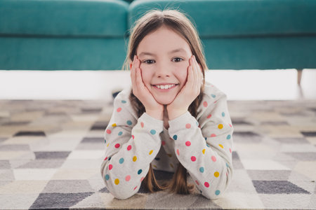 Portrait of charming little girl laying floor arms touch cheeks wear pullover modern interior flat indoorsの写真素材