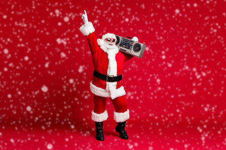 Full body size photo of retired old man grey beard hold boombox shoulder point finger up street dance wear santa costume sunglass headwear leather black boots isolated red color backgroundの写真素材