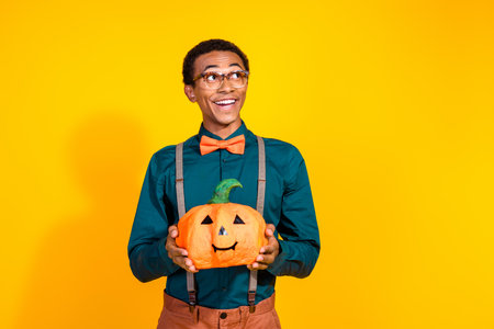 Photo of amazed guy hold pumpkin vegetable decor for halloween look empty space isolated yellow color backgroundの写真素材