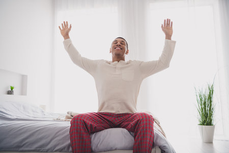 Photo of nice young man sit bed pray salute sun wear pajama enjoy wake up modern cozy interior bedroom indoorsの写真素材