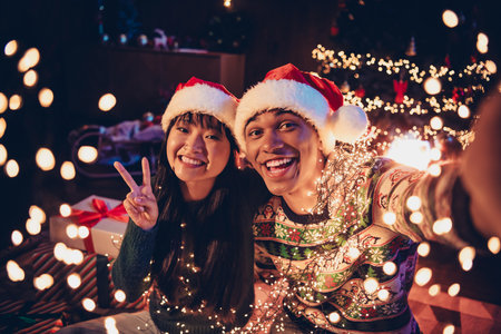 Photo of two young peaceful partners make selfie show v-sign festive christmas illumination apartment indoorsの写真素材