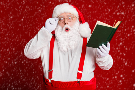 Portrait of his he attractive amazed stunned wondered fat white-haired Santa reading book education pout lips isolated over bright vivid shine vibrant red burgundy maroon color backgroundの写真素材