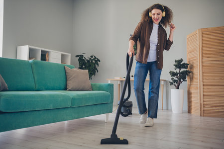 Photo of charming lady using vacuum cleaner for floor dust at her new modern loft house indoors having fun disco dance with headphonesの写真素材