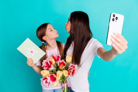 Photo of charming funny cute little girl kissing mommy mother day isolated on cyan color backgroundの写真素材