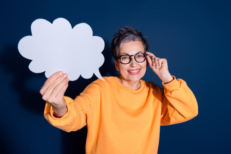Photo portrait of attractive mature woman hold paper cloud dressed stylish yellow clothes isolated on dark blue color backgroundの写真素材