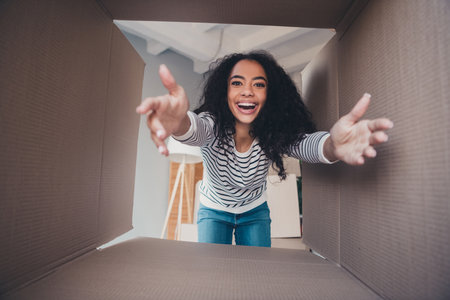 Portrait of nice young girl arms reach opened carton box package living room relocate flat indoorsの写真素材