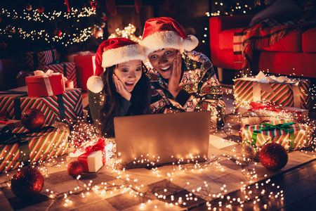 Full length photo of happy young couple lying floor amazed netbook dressed christmas garment tradition atmosphere decor house indoors roomの写真素材