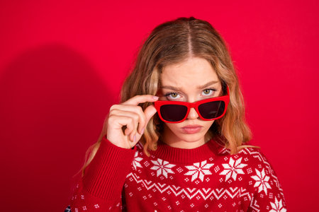 Portrait of nice young girl touch sunglass look questioned wear xmas new year sweater isolated on bright red color backgroundの写真素材