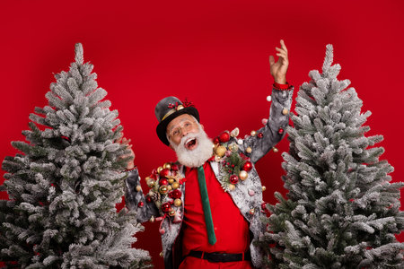 Photo of funny extravagant grandfather wear elegant stylish suit jacket sell xmas tree isolated on red color backgroundの写真素材
