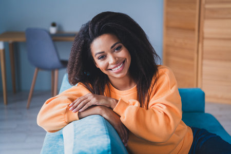 Photo of attractive young woman sit couch lean on enjoy weekend dressed orange outfit cozy day light home interior living roomの写真素材
