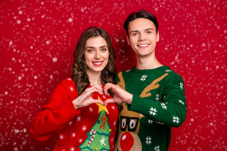 Photo of two cheerful idyllic partners touch hands fingers showing heart gesture isolated on red color backgroundの写真素材