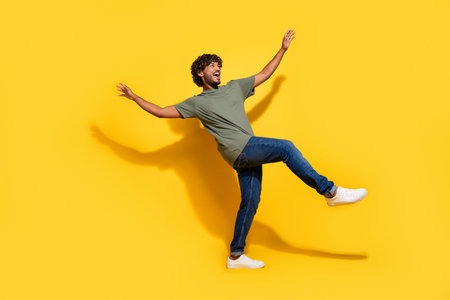 Full size photo of positive guy dressed khaki t-shirt jeans raising palms up dancing look empty space isolated on yellow color backgroundの写真素材