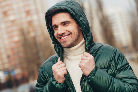 Photo of cheerful dreamy man walking on city street in cold autumn weather warm clothesの写真素材
